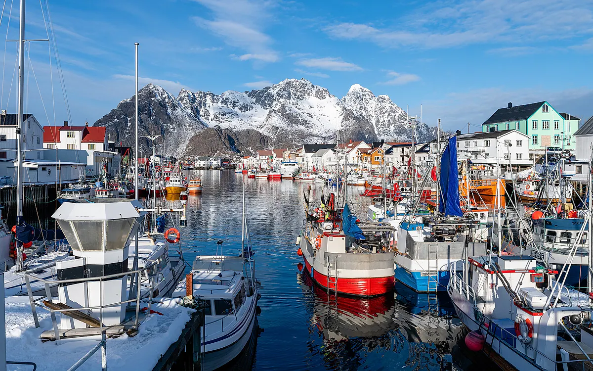 Fiskebåtene i havna i Henningsvær, med snødekte fjell bak